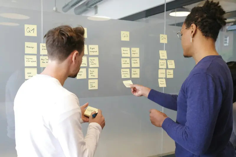Two people planning a project with sticky notes on a glass wall