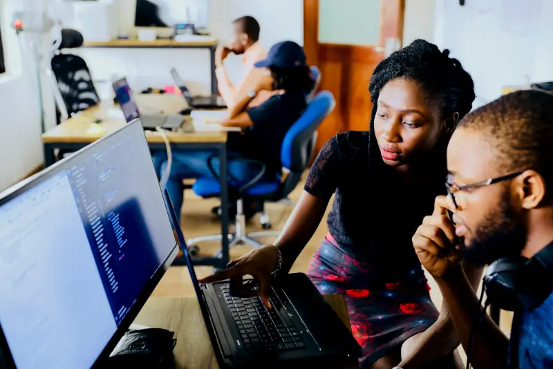 Two engineers reviewing code together on a laptop in a shared office